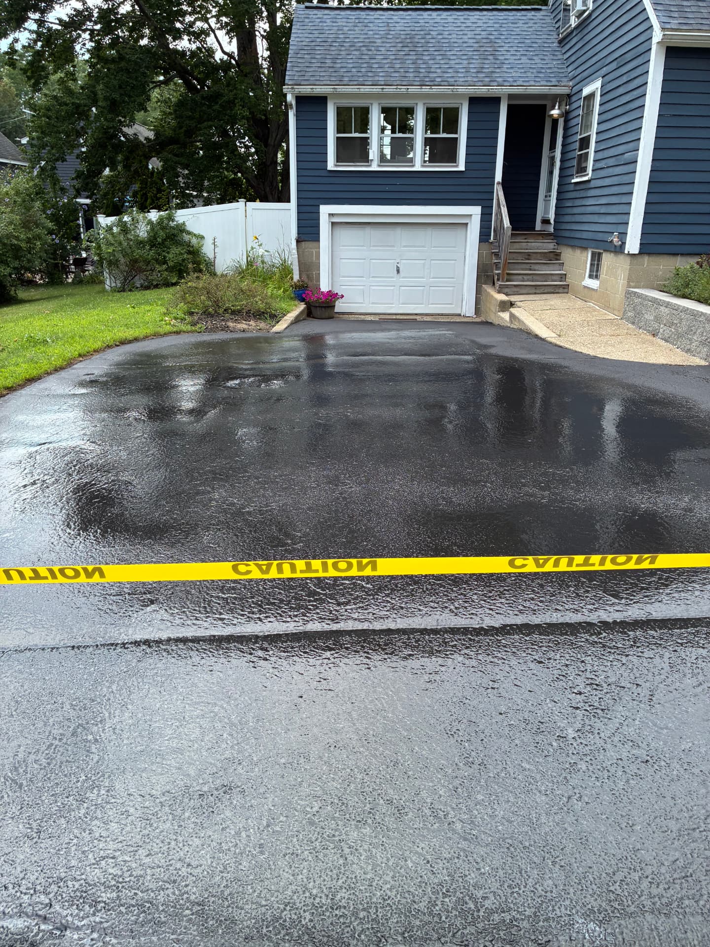 Freshly sealcoated driveway taped off with caution tape to cure in front of a navy blue home