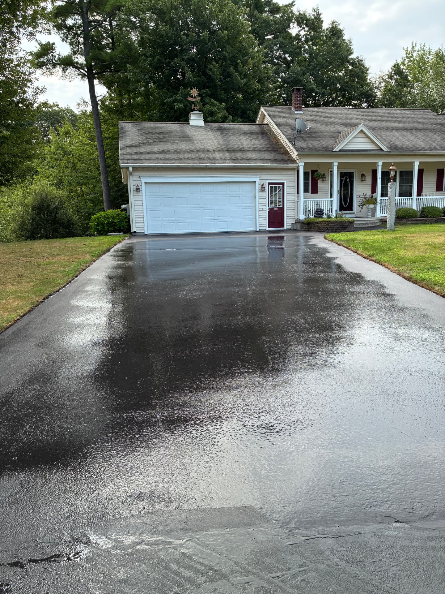 Newly sealcoated asphalt driveway leading to a white garage door on a Maine ranch home