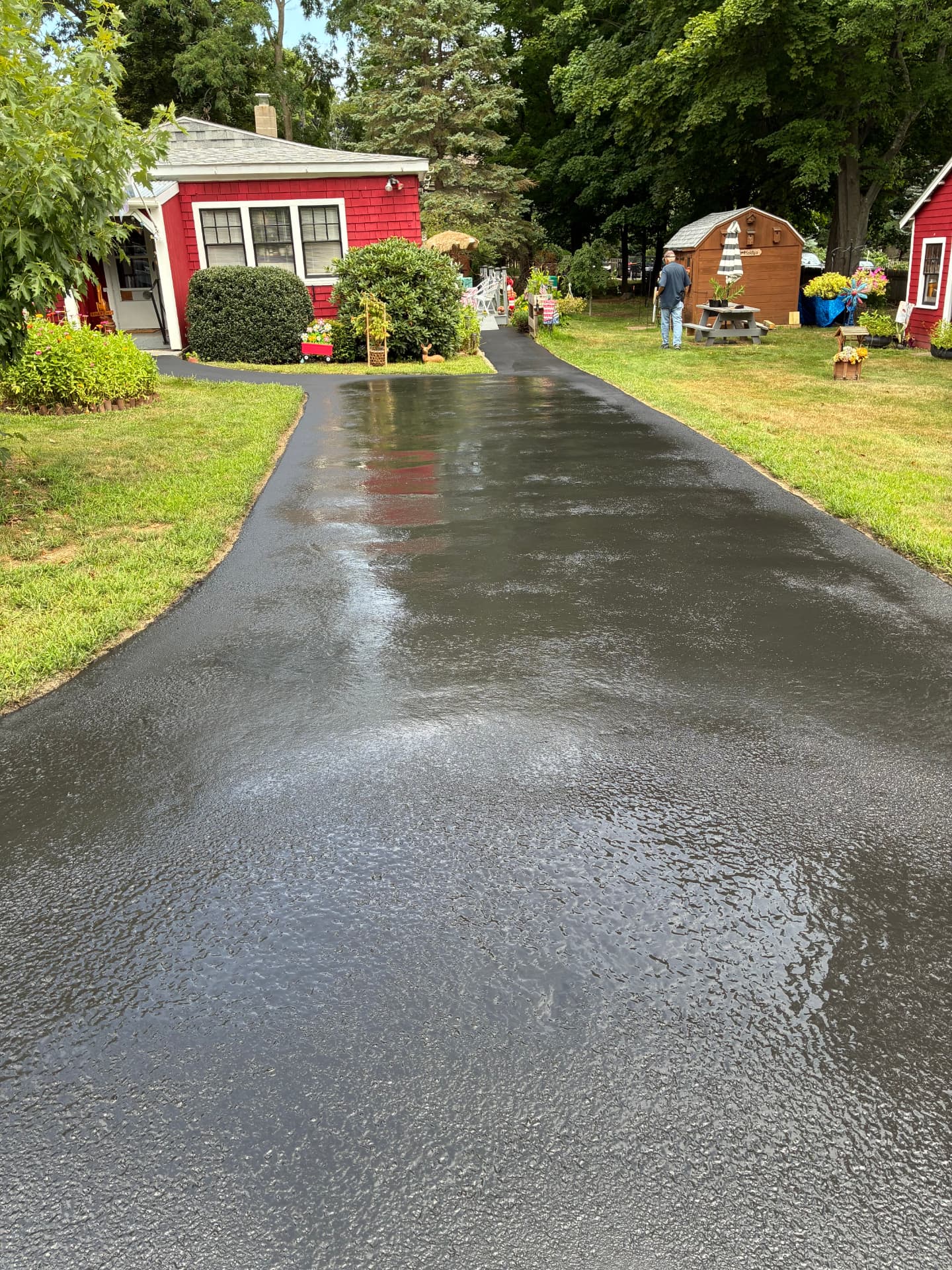 Long freshly sealcoated asphalt driveway beside a red cottage and lawn in southern Maine